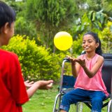 Happy young brother playing with his sister while using wheelchair at park - concept of happiness, inspirational and family support.
