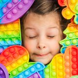Little girl,kid,child head among many,lots of colorful pop it. Children play. Trendy silicone antistress colorful sensory push toy popit. Flapping fidget. Rainbow color.Cure of autism.Stress reliever.